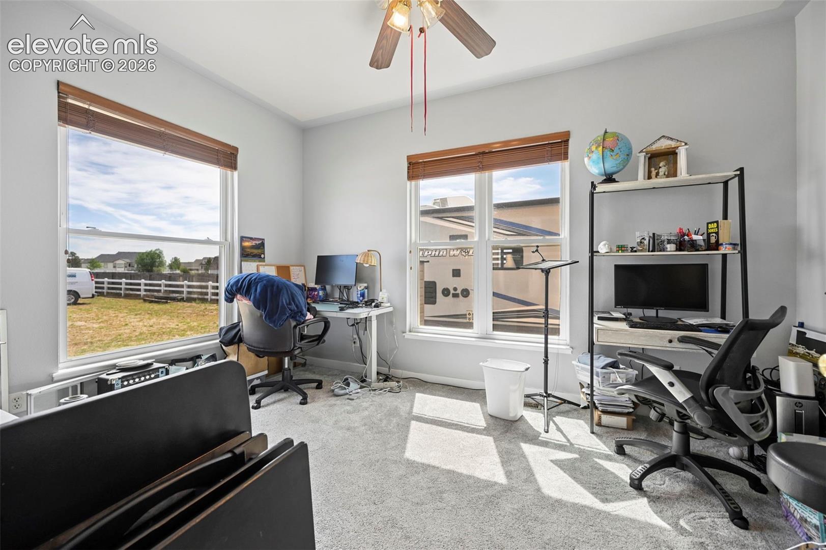 8347 Tibbs Road Peyton, CO 80831 - Photo 19 of 38 Carpeted room with light gray walls, two large windows with horizontal blinds, and a ceiling fan with integrated lighting