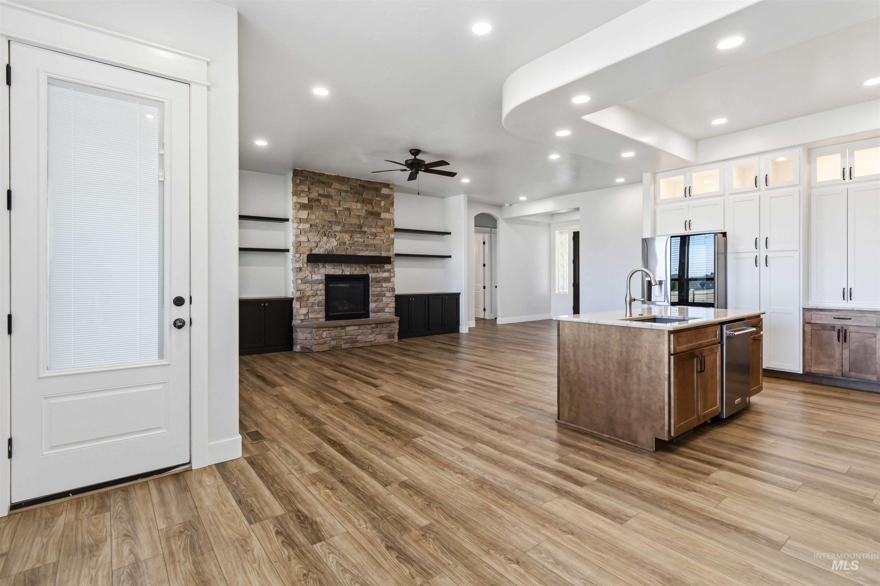 3218 North Cherry Laurel Way Star, ID 83669 - Photo 11 of 50 Open-concept living space featuring a central island with a sink and integrated dishwasher, wood-finish flooring, a stone-clad fireplace with a dark mantel, built-in shelving, and recessed lighting