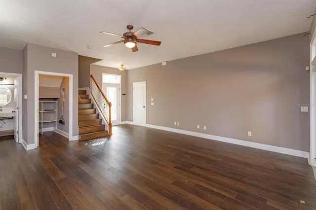 a view of an empty room with wooden floor stairs and a ceiling fan