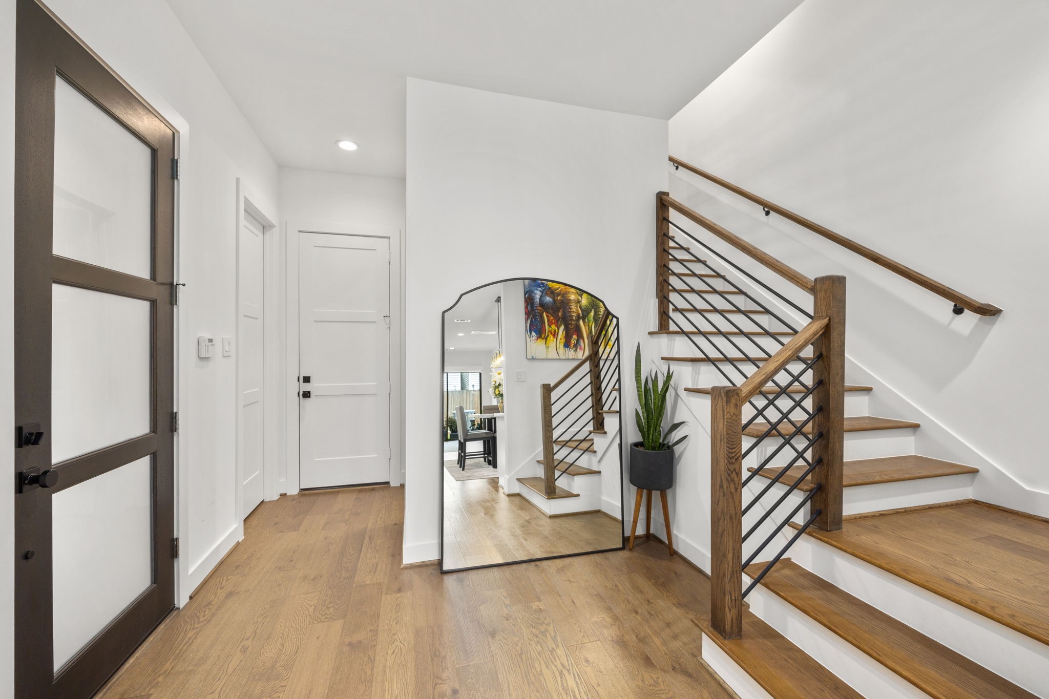 2411 Hazard Street Houston, TX 77019 - Photo 10 of 46 This bright and welcoming foyer features a stylish blend of modern and rustic elements, including warm wood flooring, a sleek black-framed mirror, and contemporary iron staircase railing. The thoughtfully placed accent pieces and natural lighting create an inviting first impression that seamlessly flows into the rest of the home.
