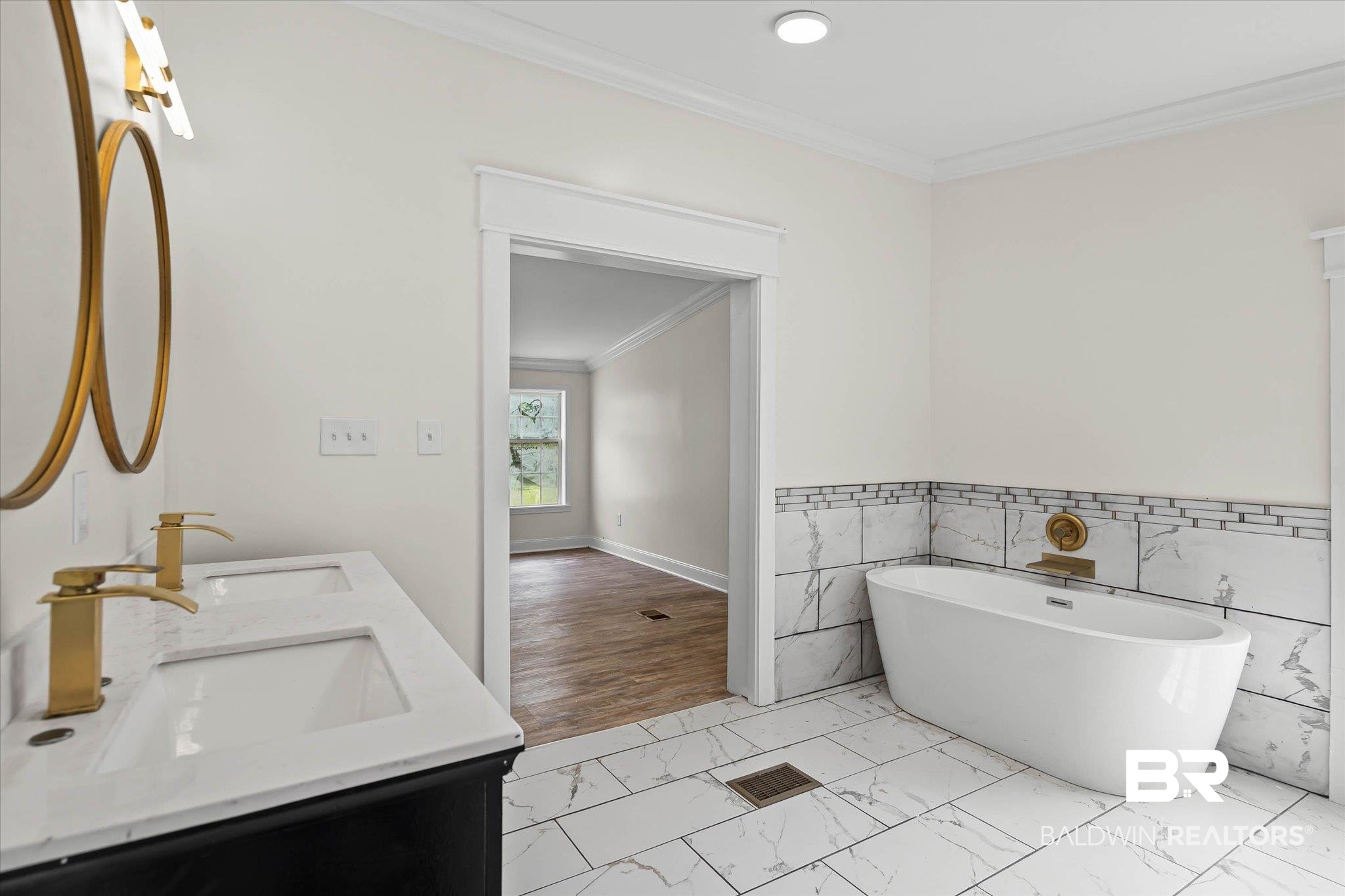 9230 McLeod Road Mobile, AL 36695 - Photo 13 of 20 Bathroom featuring a freestanding soaking tub with brass fixtures, a dual vanity with rectangular undermount sinks and brass faucets, and marble-look tile flooring