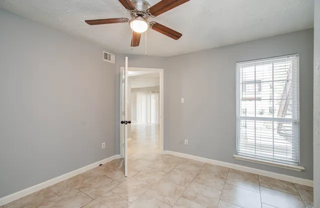 an empty room with chandelier fan and windows