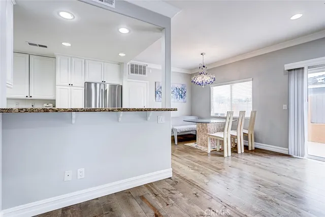 a kitchen with stainless steel appliances granite countertop a refrigerator a sink dishwasher a stove and a dining table with wooden floor