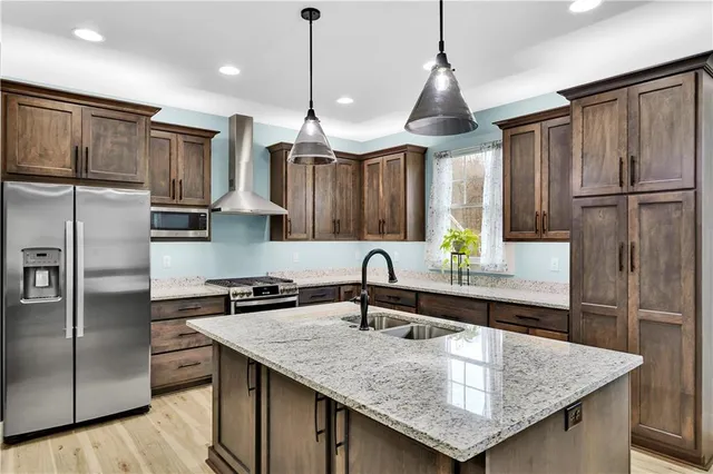 a kitchen with stainless steel appliances granite countertop a sink a refrigerator and a wooden floor