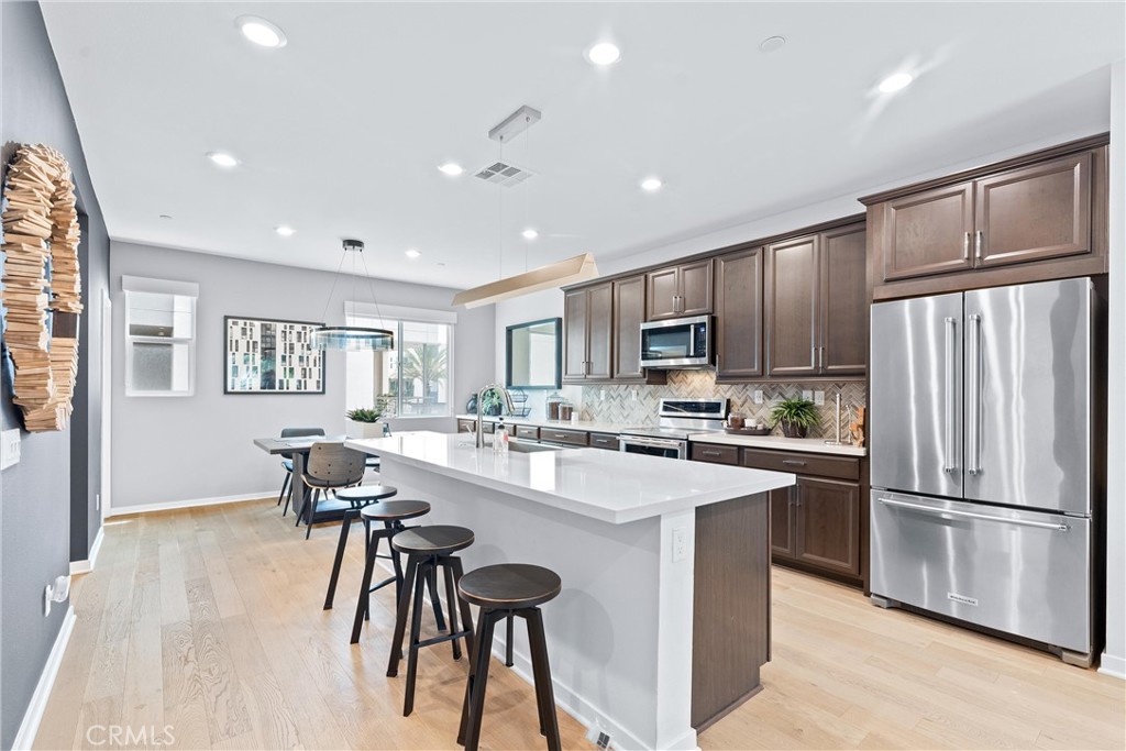 134 Citysquare Irvine, CA 92614 - Photo 11 of 32 a kitchen with stainless steel appliances granite countertop a refrigerator a stove a sink a dining table and chairs with wooden floor