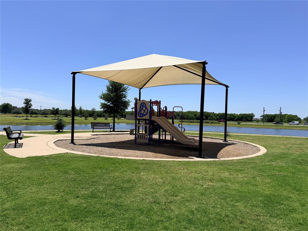 816 Country Road Royse City, TX 75189 - Photo 20 of 24 Playground structure with shade canopy, adjacent to a pond with a concrete pathway and green space