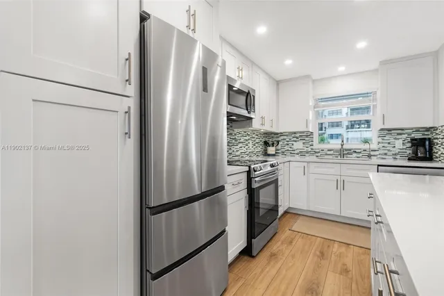 a kitchen with stainless steel appliances a refrigerator a sink and white cabinets