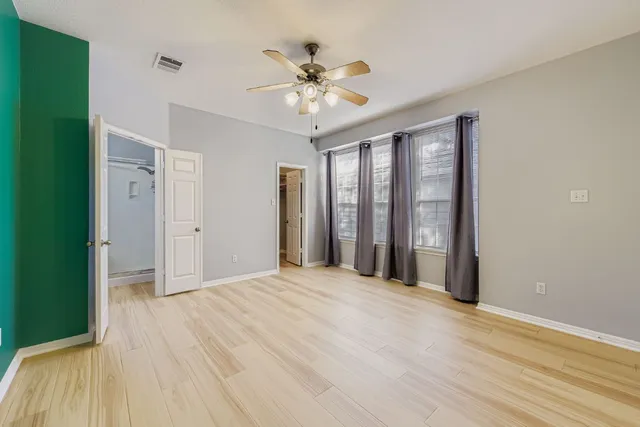 a view of an empty room with wooden floor and a ceiling fan