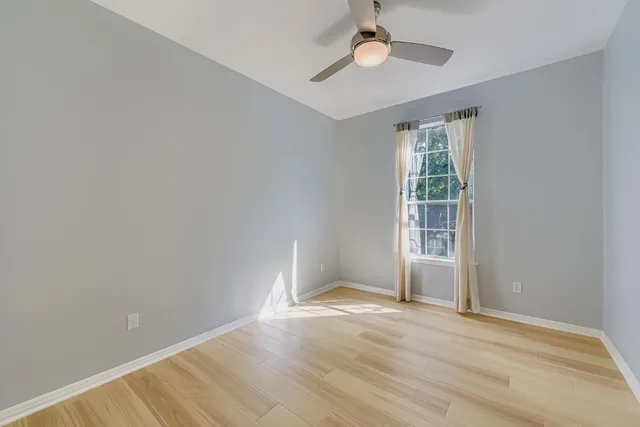 an empty room with wooden floor chandelier fan and windows