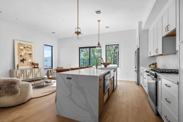 a large kitchen with stainless steel appliances granite countertop a stove a sink dishwasher a refrigerator and a wooden floor