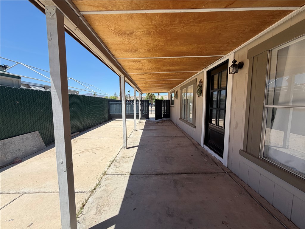 1910 Rio Grande Road Bullhead City, AZ 86442 - Photo 26 of 29 Covered concrete patio extending along the side of the structure, featuring a wood-finish ceiling and metal support posts