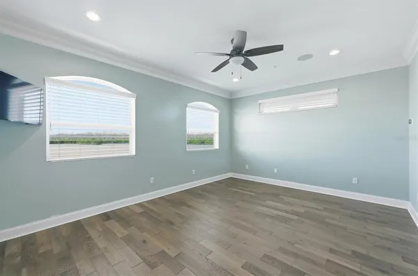 an empty room with wooden floor ceiling fan and windows