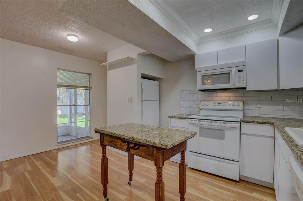 864 Lake Haven Road Dunedin, FL 34698 - Photo 4 of 28 a kitchen with granite countertop a stove a sink and white cabinets with wooden floor