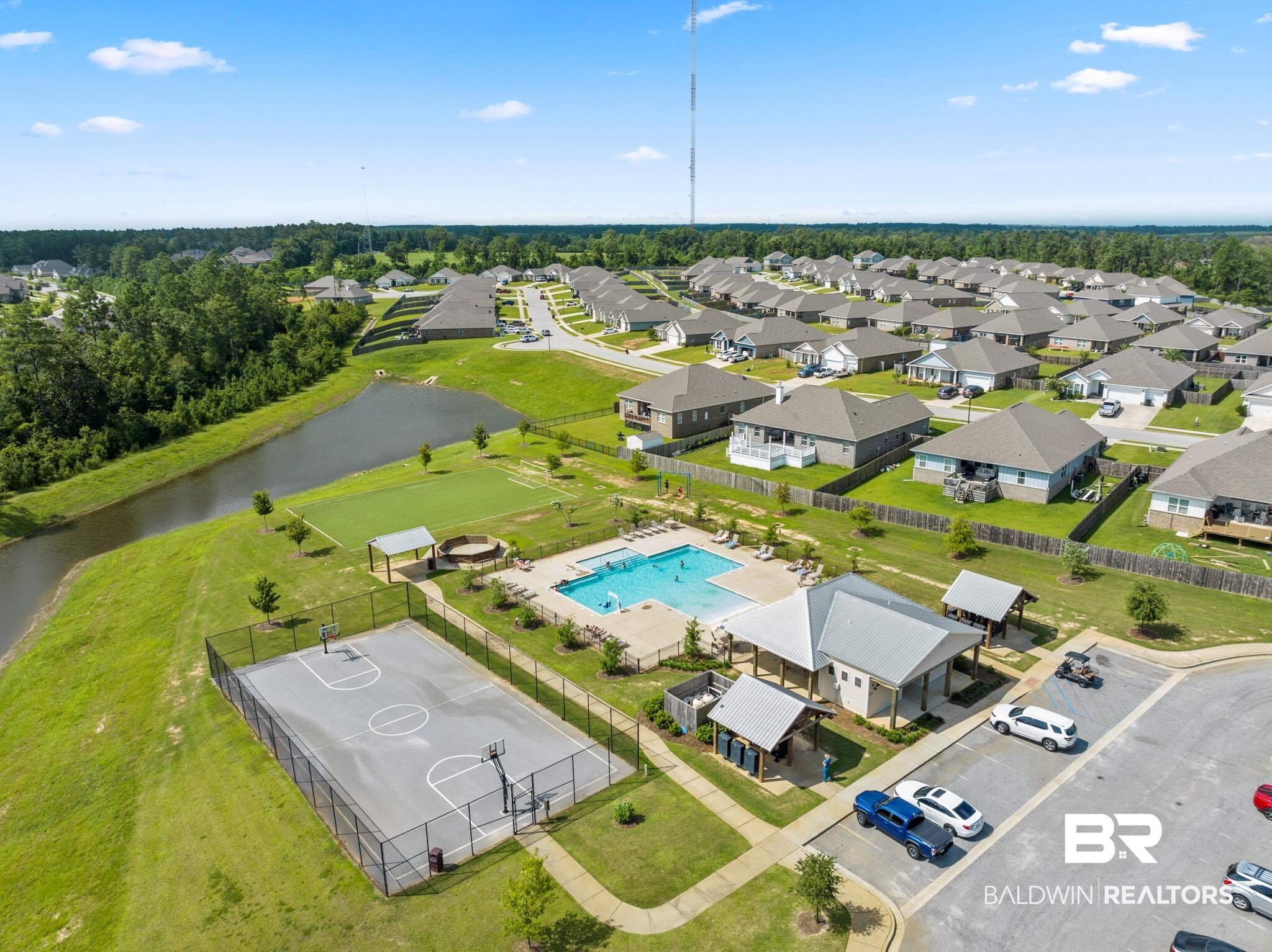 32125 Lyon Road Daphne, AL 36527 - Photo 44 of 70 Community amenities featuring a fenced basketball court, a recreational pool with surrounding lounge chairs, a clubhouse with covered outdoor seating, a green space, and a pond