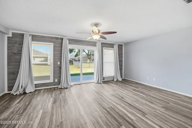 an empty room with wooden floor chandelier fan and windows