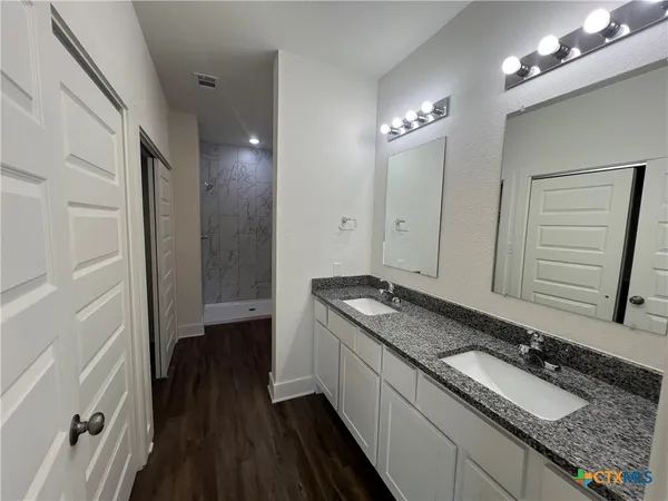 a bathroom with a granite countertop double vanity sink a mirror and a shower
