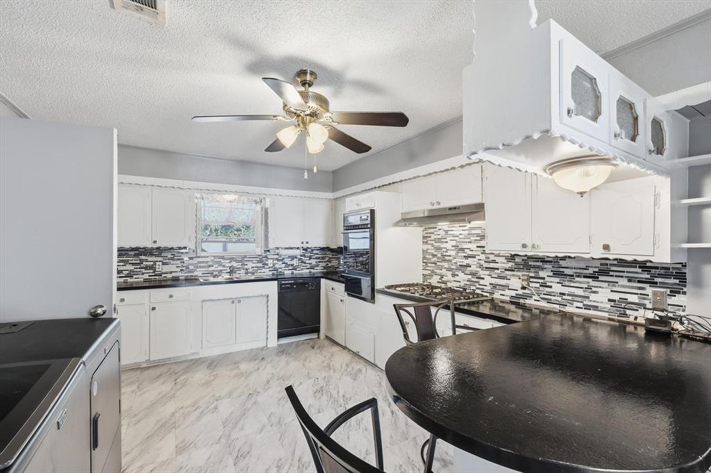 910 Rockwall Street McKinney, TX 75069 - Photo 10 of 34 Kitchen featuring dark countertops, a textured ceiling, white cabinets, light marble finish floors, and black appliances