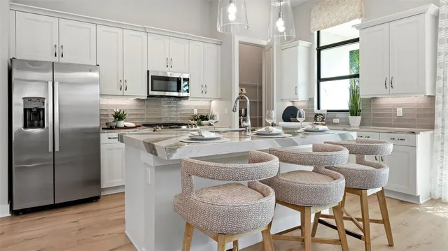 a kitchen with stainless steel appliances granite countertop a sink a stove a refrigerator cabinets and chairs