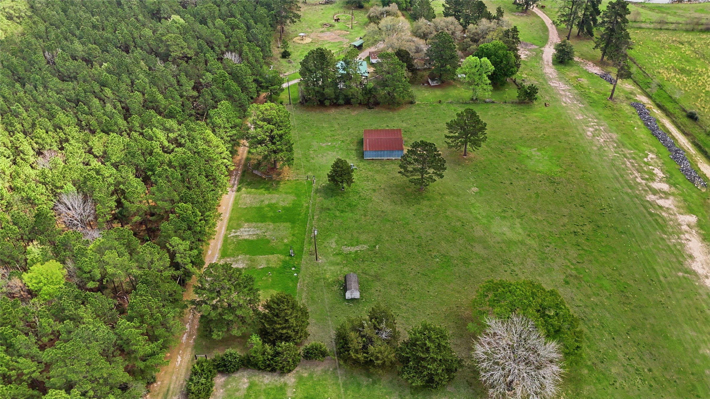 872 Four Notch Road Huntsville, TX 77340 - Photo 23 of 42 Expansive rural property surrounded by lush greenery, featuring a central barn and a charming driveway leading to a hidden home amidst mature trees.