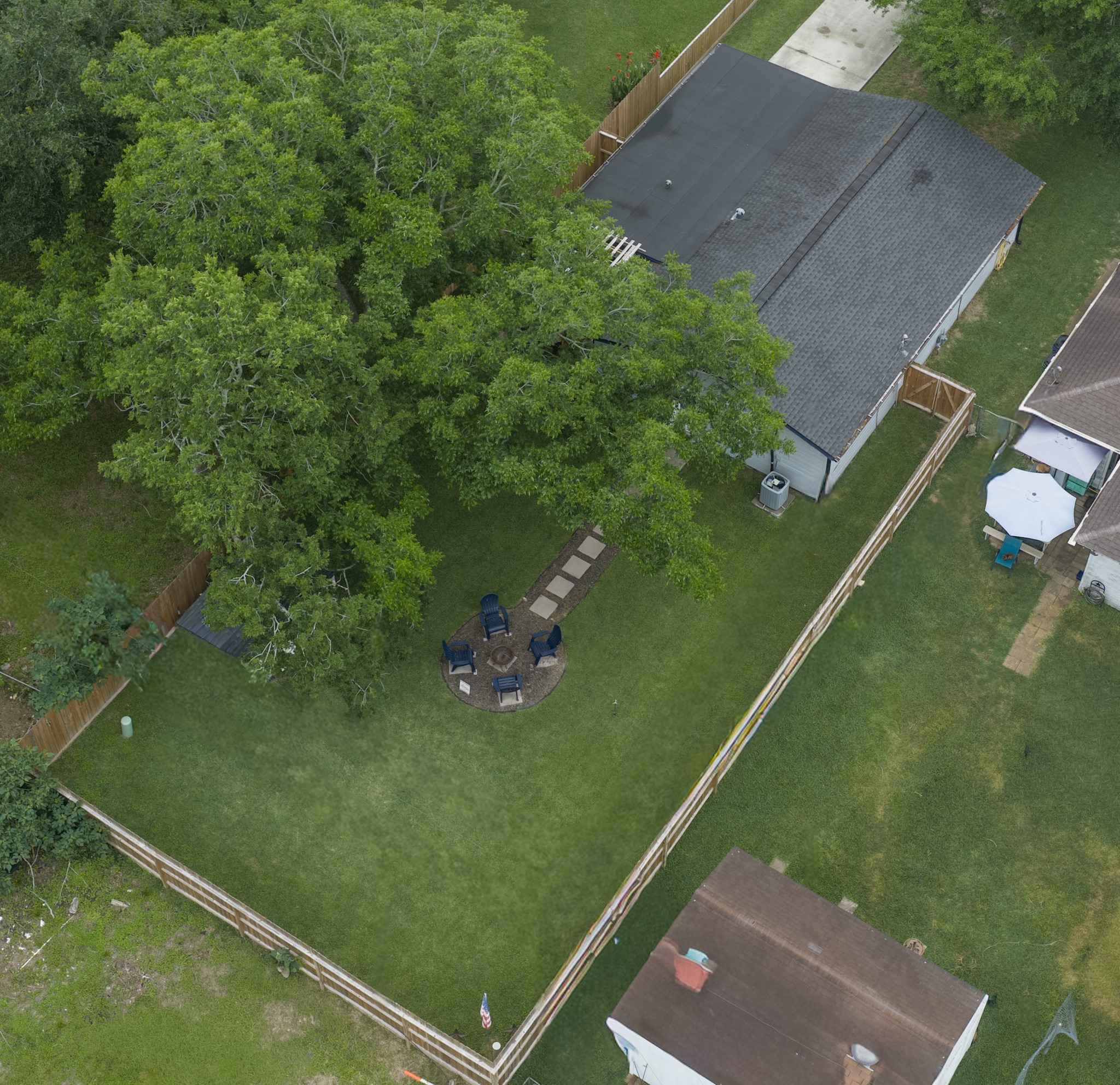 846 South Anderson Street Angleton, TX 77515 - Photo 29 of 30 This aerial view shows a cozy backyard with a well-maintained lawn, a fenced perimeter, and a large tree providing shade. There's a circular seating area with chairs and a fire pit, perfect for outdoor gatherings. The property is adjacent to neighboring homes, offering a sense of community while maintaining privacy.