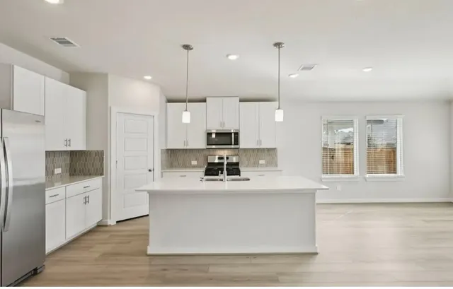a large white kitchen with kitchen island a stove a sink a refrigerator and white cabinets with wooden floor