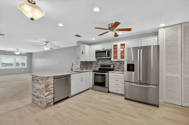 a kitchen with stainless steel appliances kitchen island granite countertop a refrigerator oven a sink dishwasher and white cabinets with wooden floor