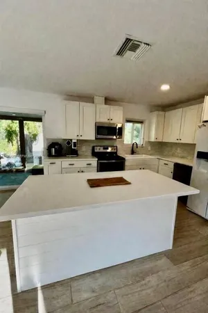 a large kitchen with stainless steel appliances a stove a sink a refrigerator a center island and cabinets