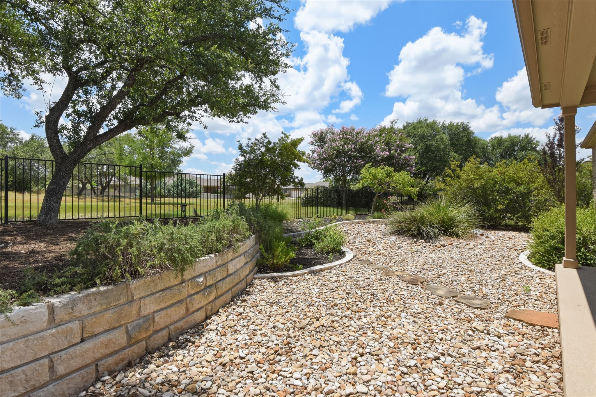 104 Coffee Mill Creek Road Georgetown, TX 78633 - Photo 32 of 40 A well-landscaped yard features a stone retaining wall and decorative gravel, bordered by mature trees and a sturdy fence.