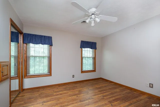 an empty room with wooden floor chandelier fan and windows