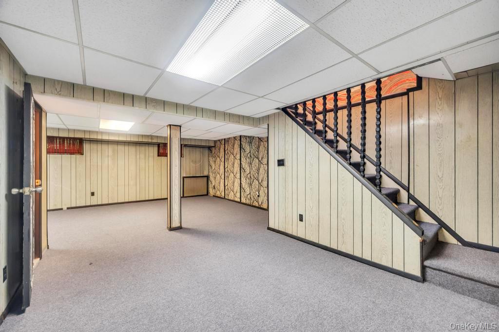 51 Stevenson Road Hewlett, NY 11557 - Photo 17 of 21 Finished basement featuring wooden walls, carpet floors, a drop ceiling, and stairway