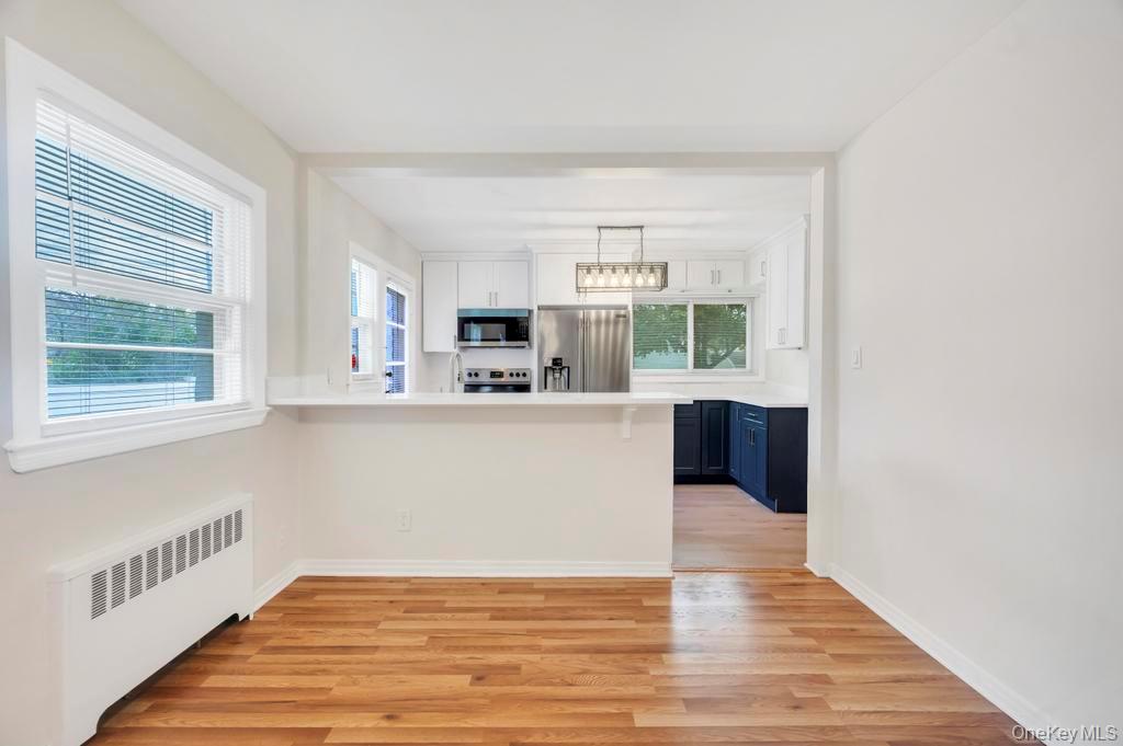 51 Stevenson Road Hewlett, NY 11557 - Photo 3 of 21 Kitchen with radiator heating unit, white cabinetry, light wood-type flooring, light countertops, and stainless steel appliances