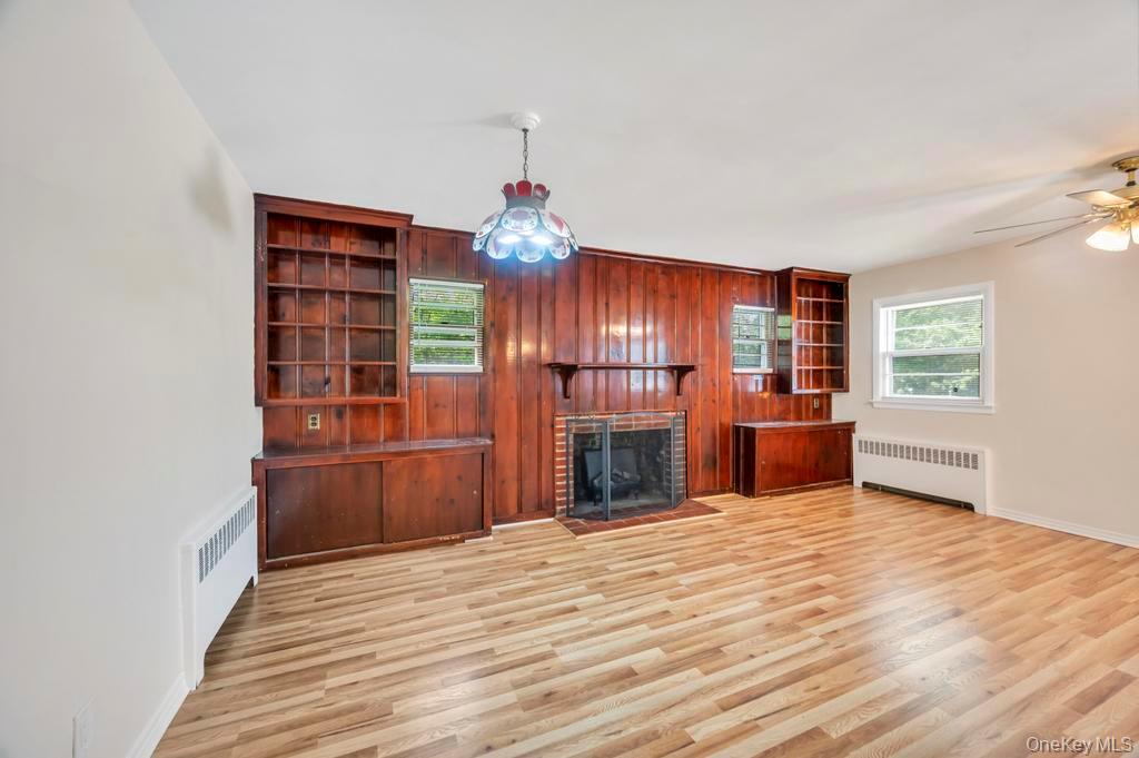 51 Stevenson Road Hewlett, NY 11557 - Photo 6 of 21 Unfurnished living room with wooden walls, radiator, light wood-style floors, and a brick fireplace