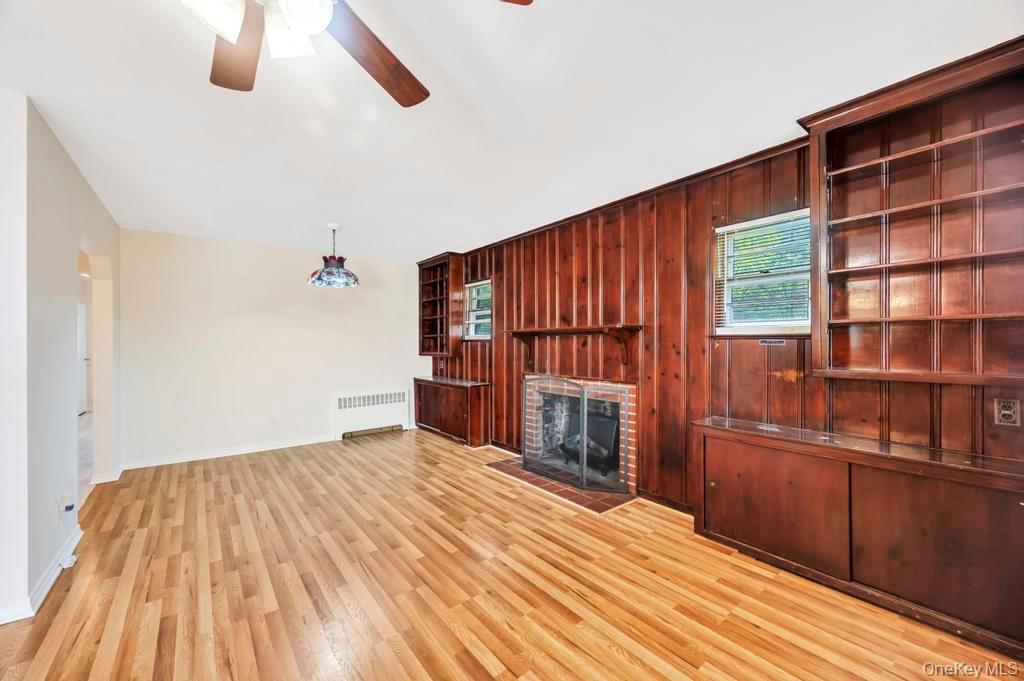 51 Stevenson Road Hewlett, NY 11557 - Photo 9 of 21 Unfurnished living room featuring wooden walls, a fireplace, radiator, light wood-style floors, and a ceiling fan