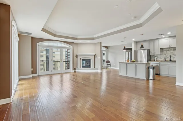 a view of an empty room with wooden floor and a kitchen