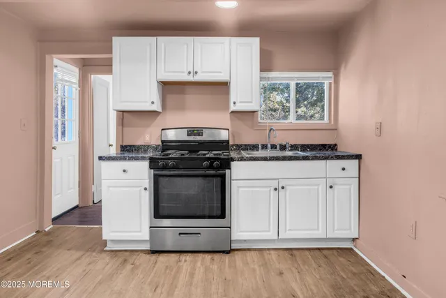 a kitchen with granite countertop white cabinets appliances a sink and a window