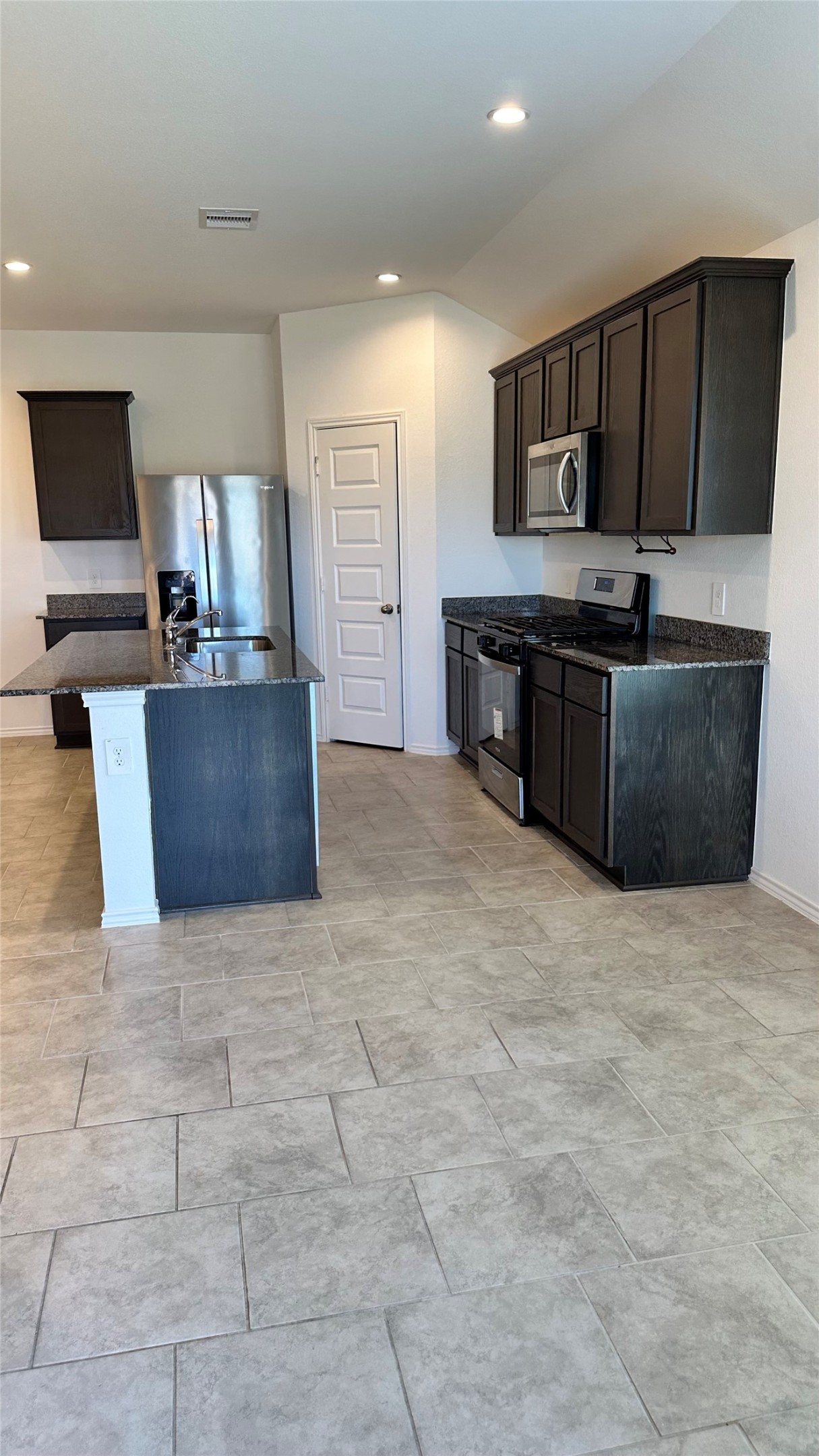 1103 Cattle Chute Court Rosharon, TX 77583 - Photo 10 of 26 Modern kitchen with dark wood cabinets, granite countertops, and stainless steel appliances. Features an island with a sink and ample tiled floor space, providing a clean and functional cooking area.