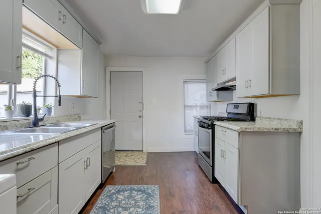 a kitchen with a sink dishwasher a stove and white cabinets with wooden floor