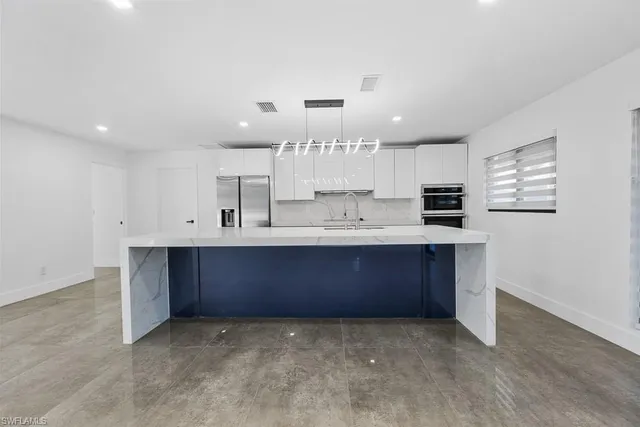 a large kitchen with a large counter top a sink stainless steel appliances and cabinets