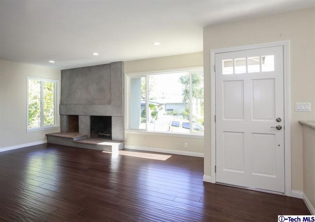 an empty room with wooden floor fireplace and windows