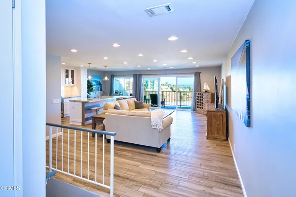 a living room with stainless steel appliances furniture wooden floor and a large window