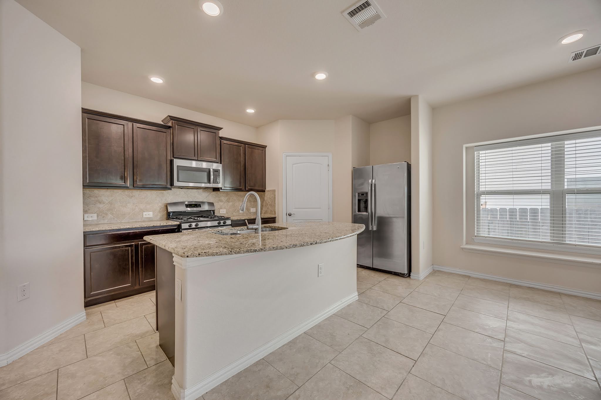 7212 Vail Ridge Street Austin, TX 78744 - Photo 2 of 26 A well-appointed kitchen features dark wood cabinetry, granite countertops, and modern stainless steel appliances.
