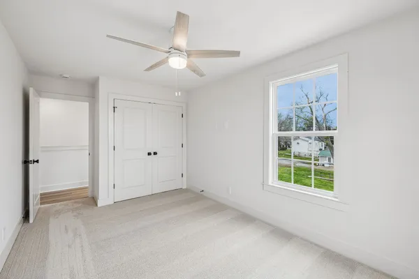 an empty room with wooden floor chandelier fan and windows