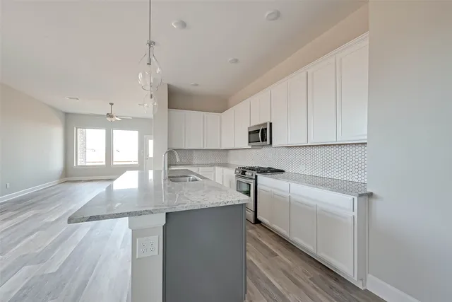 a kitchen with stainless steel appliances granite countertop a sink a stove and white cabinets with wooden floor