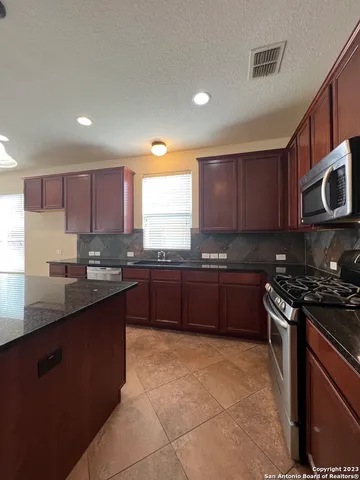 a large kitchen with granite countertop wooden cabinets and a stove top oven