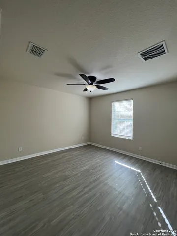 an empty room with wooden floor ceiling fan and windows