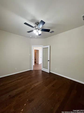 a view of an empty room with wooden floor and a ceiling fan
