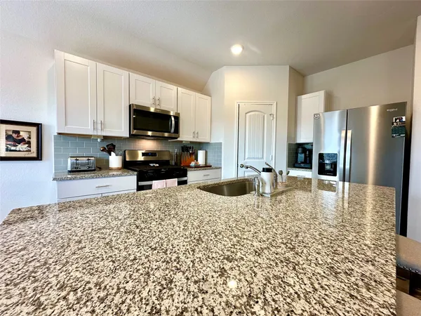 a kitchen with granite countertop a stove a sink and a refrigerator