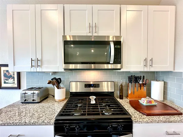 a kitchen with granite countertop a stove a sink and white cabinets