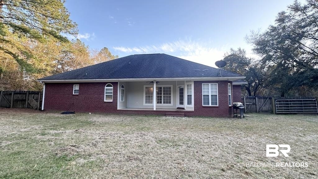 23289 McPhillips Road Loxley, AL 36551 - Photo 15 of 19 Expansive backyard featuring a red brick exterior with white trim, a covered patio with recessed lighting, multiple windows, and a dark shingle roof
