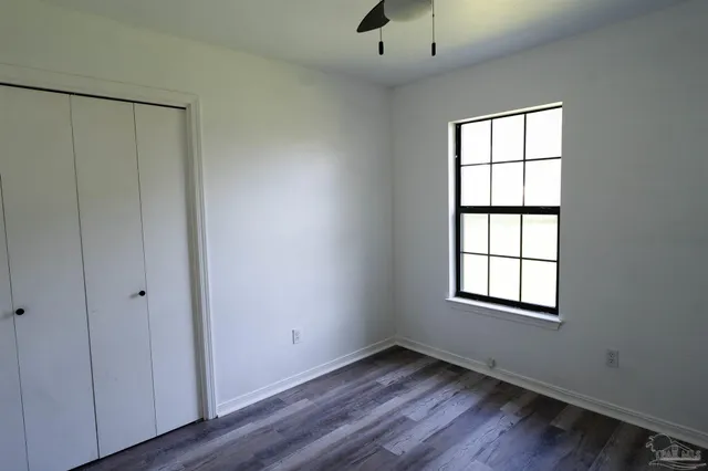 an empty room with wooden floor closet and windows